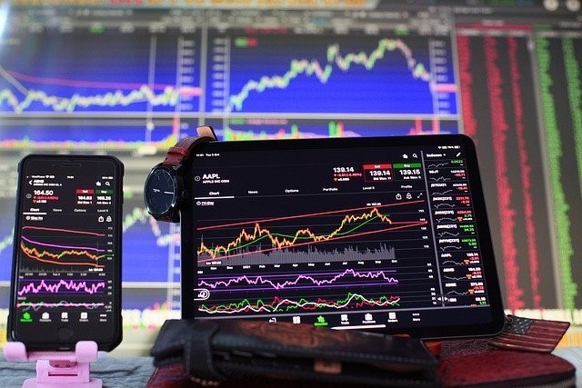A picture showing forex charts on a tablet and phone screen with more charts in the background